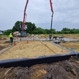 SM BUILDINGS SPÓŁKA Z OGRANICZONĄ ODPOWIEDZIALNOŚCIĄ - Wylewanie betonu na przygotowany fundament z izolacją, widoczny betonowóz z pompą i pracownicy wyrównujący beton.