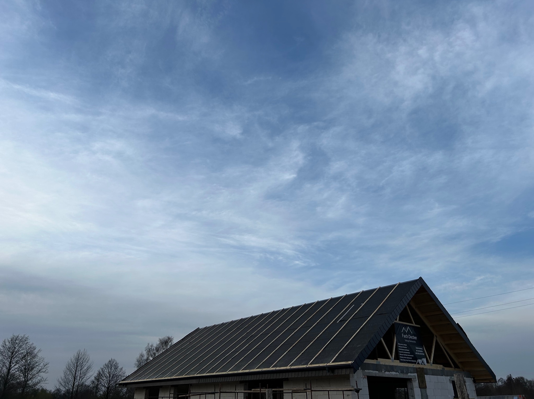 Nowy dach z czarnej papy na budynku w trakcie budowy, widoczne drewniane łaty, tło stanowi pochmurne niebo