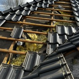 PLEPLO SPÓŁKA Z OGRANICZONĄ ODPOWIEDZIALNOŚCIĄ - Czarny dach z widoczną izolacją z wełny mineralnej i elementami drewnianymi, częściowo pokryty dachówką. Fragment dachu w trakcie naprawy lub ocieplania.