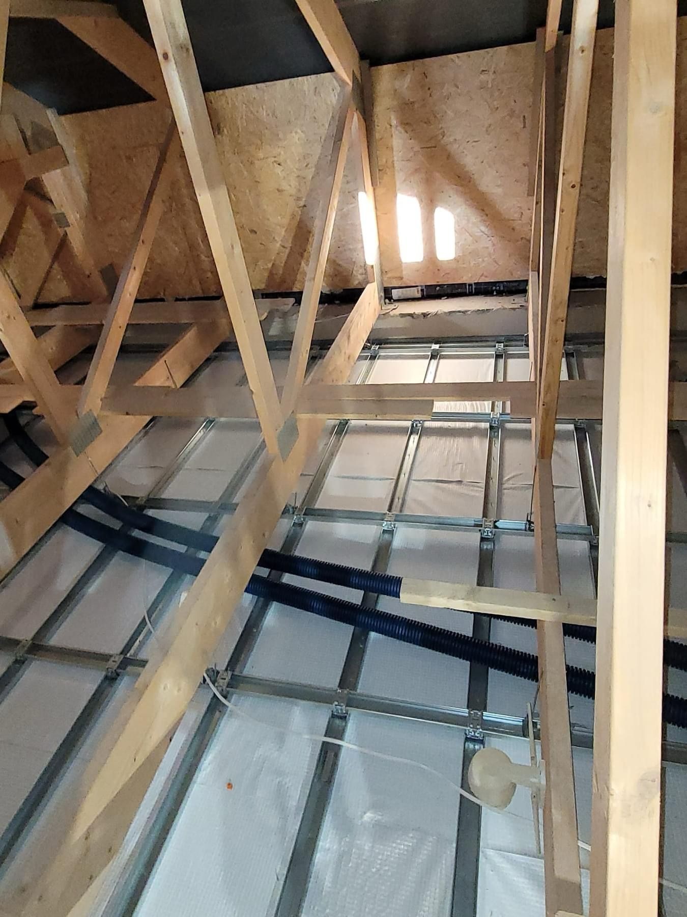 Konstrukcja drewniana poddasza z widoczną instalacją i izolacją folią aluminiową oraz fragmentem oświetlenia.