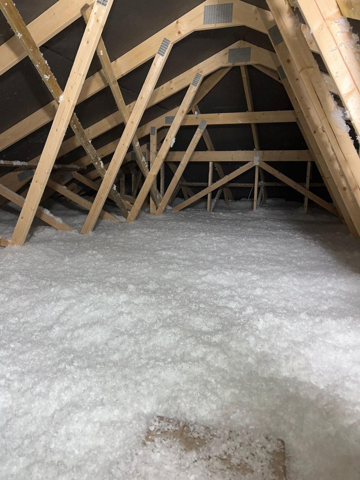 Poddasze z drewnianą konstrukcją krokwi wypełnione białą, puszystą izolacją, widoczne metalowe łączniki krokwi, ciemne poszycie dachu.