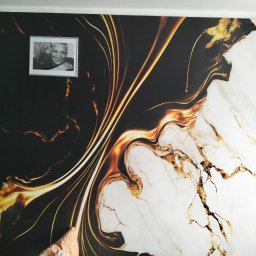 Mat bud profesinal - Czarno-białe zdjęcie pary w ramce zawieszone na ścianie z tapetą imitującą marmur z żyłami w kolorze złota.