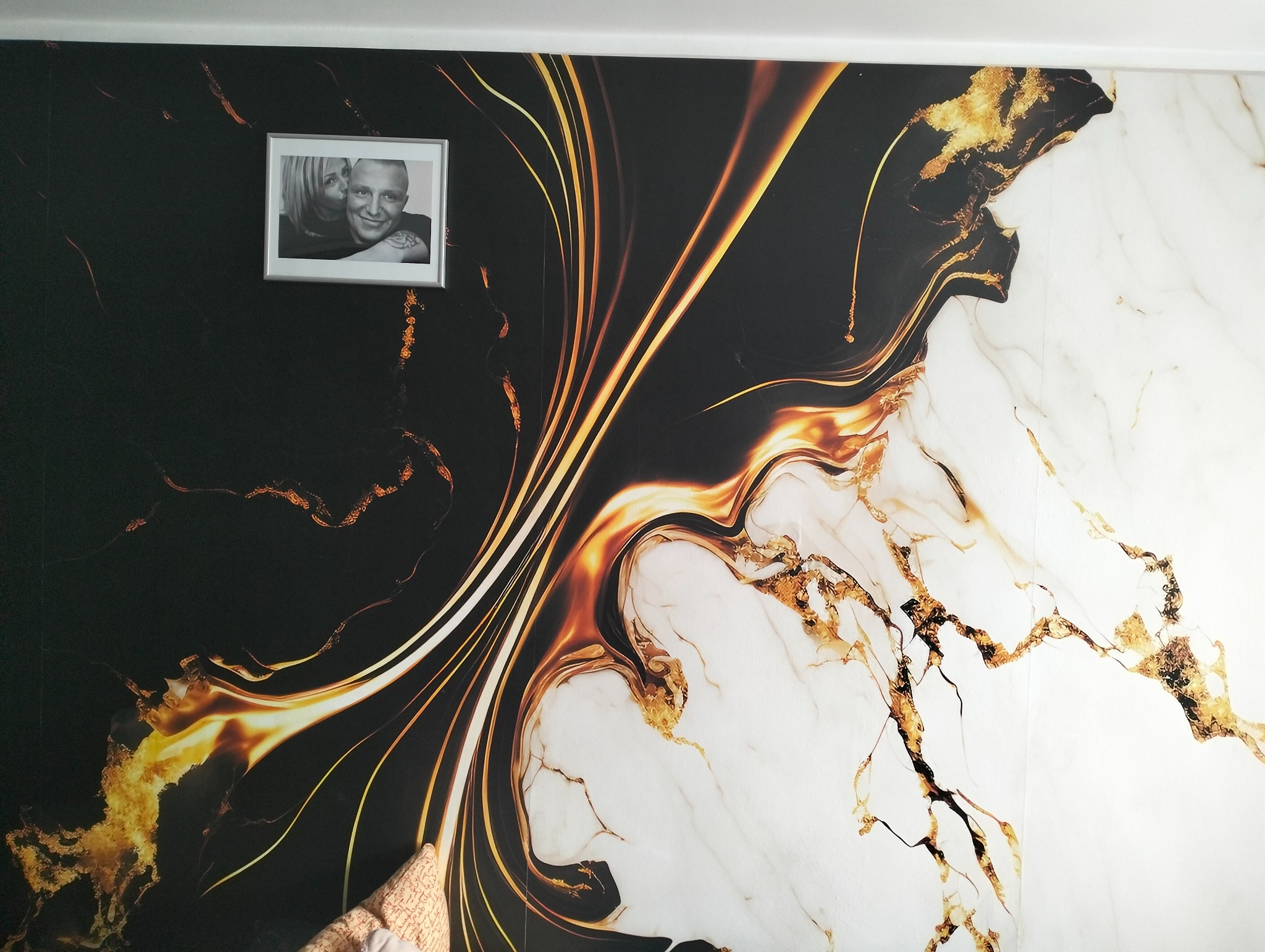 Czarno-białe zdjęcie pary w ramce zawieszone na ścianie z tapetą imitującą marmur z żyłami w kolorze złota.