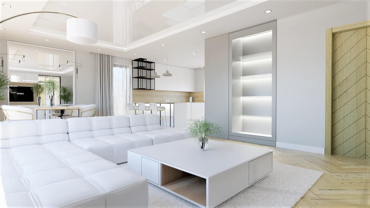 Jasne, przestronne wnętrze salonu z aneksem kuchennym, dominująca biel, duża narożna sofa, stolik kawowy z wnęką, oświetlona półka w ścianie i drewniane drzwi z wzorem jodełki na podłodze.