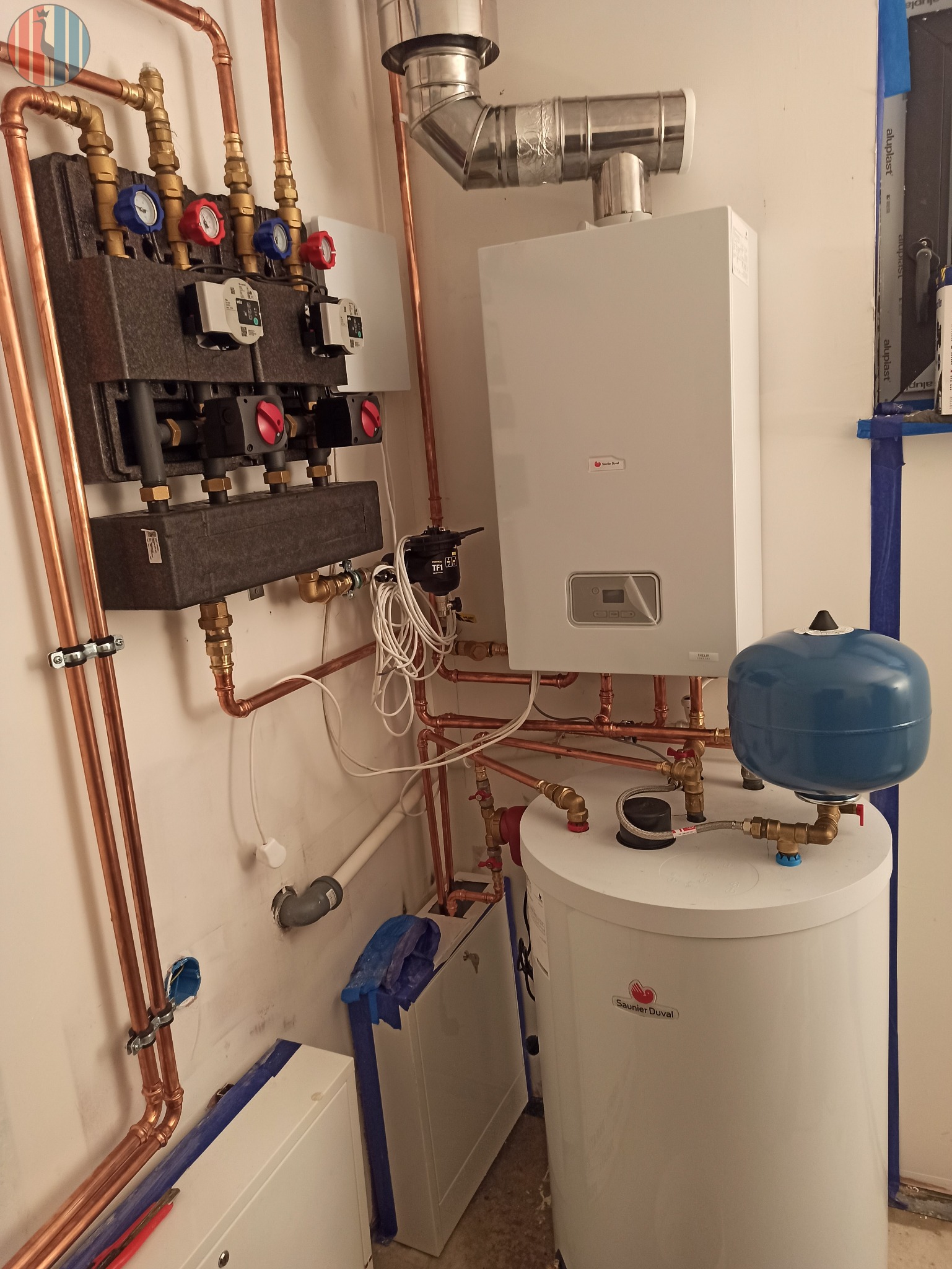 Węzeł cieplny z rozdzielaczem, piecem gazowym i zasobnikiem ciepłej wody użytkowej Saunier Duval, połączone miedzianymi rurami w kotłowni.