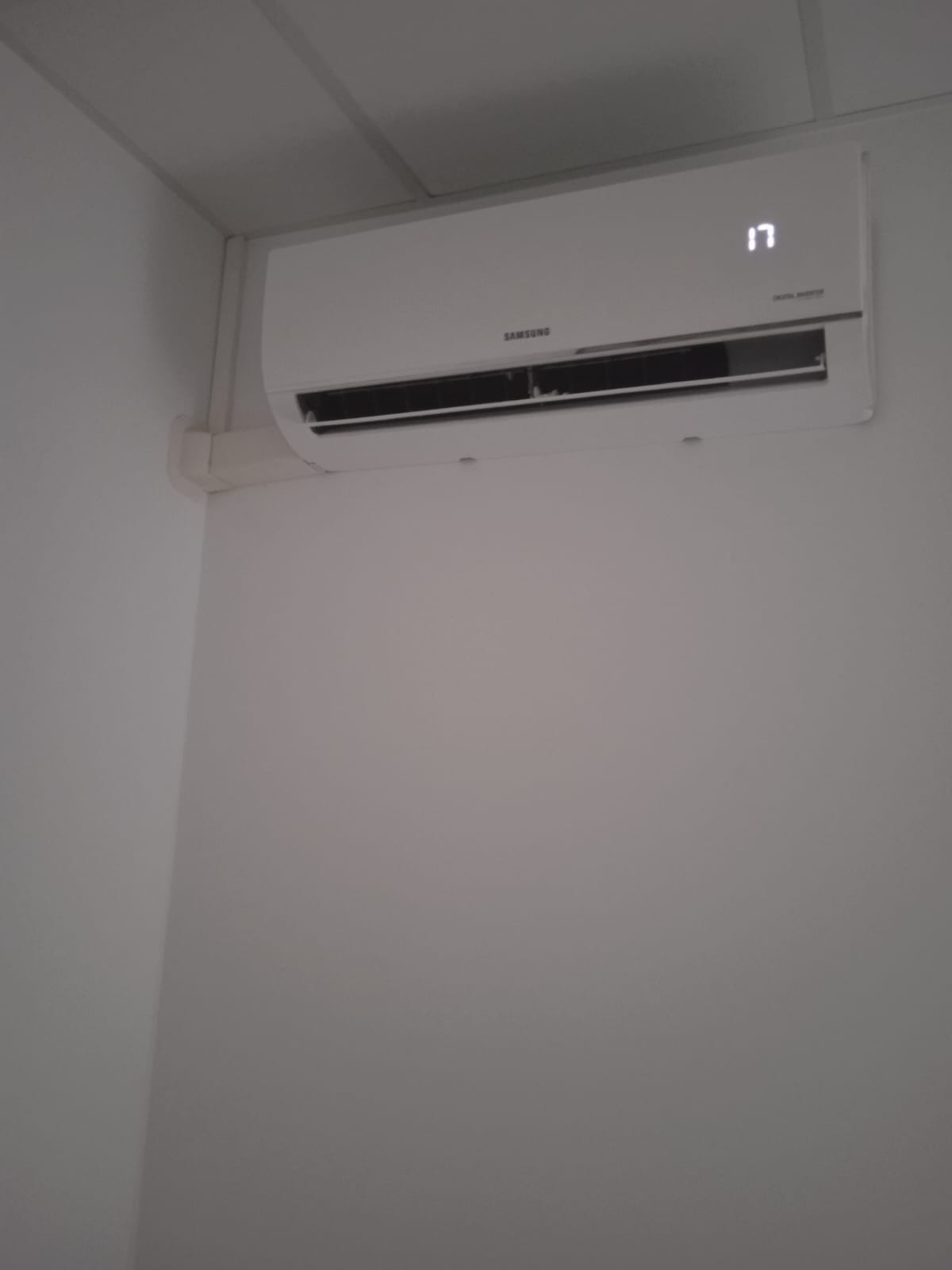 Biały klimatyzator Samsung z wyświetlaczem temperatury 17 stopni Celsjusza, zamontowany na białej ścianie w rogu pomieszczenia.