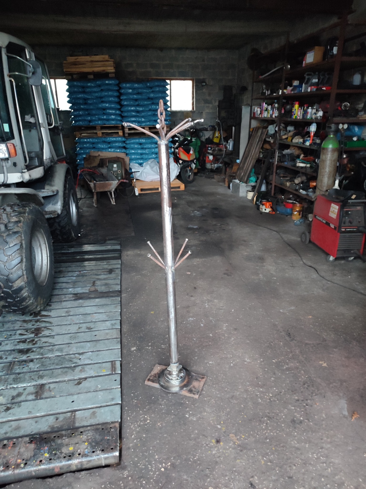 Metalowy wieszak na ubrania, wykonany w warsztacie, z widocznym spawarką i stertą worków w tle.
