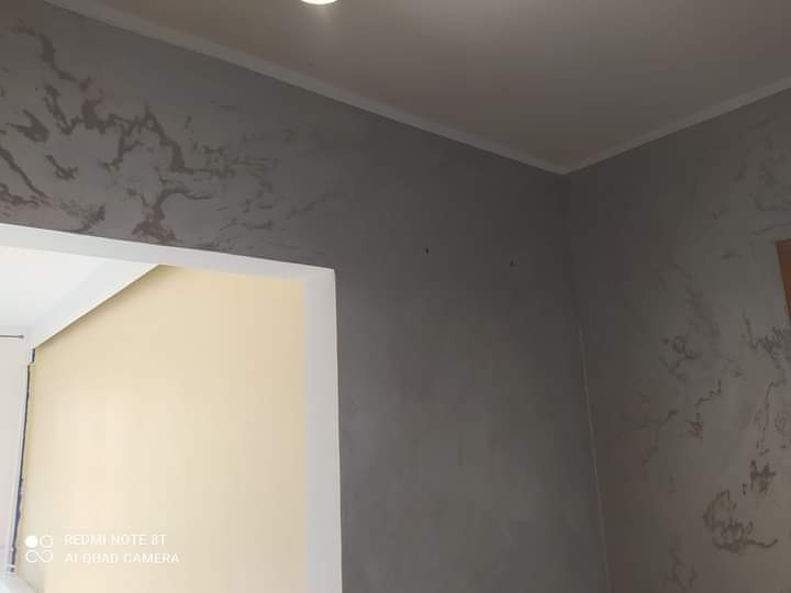 Ściana w pokoju po nałożeniu dekoracyjnej szarej farby z efektem marmuru, widoczna listwa przysufitowa i fragment ościeżnicy.