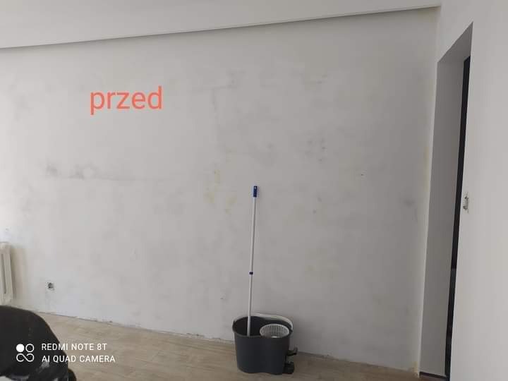 Pokój przed remontem: surowa ściana, widoczna niedoskonałość powierzchni, mop w wiadrze i napis 'przed' na ścianie.