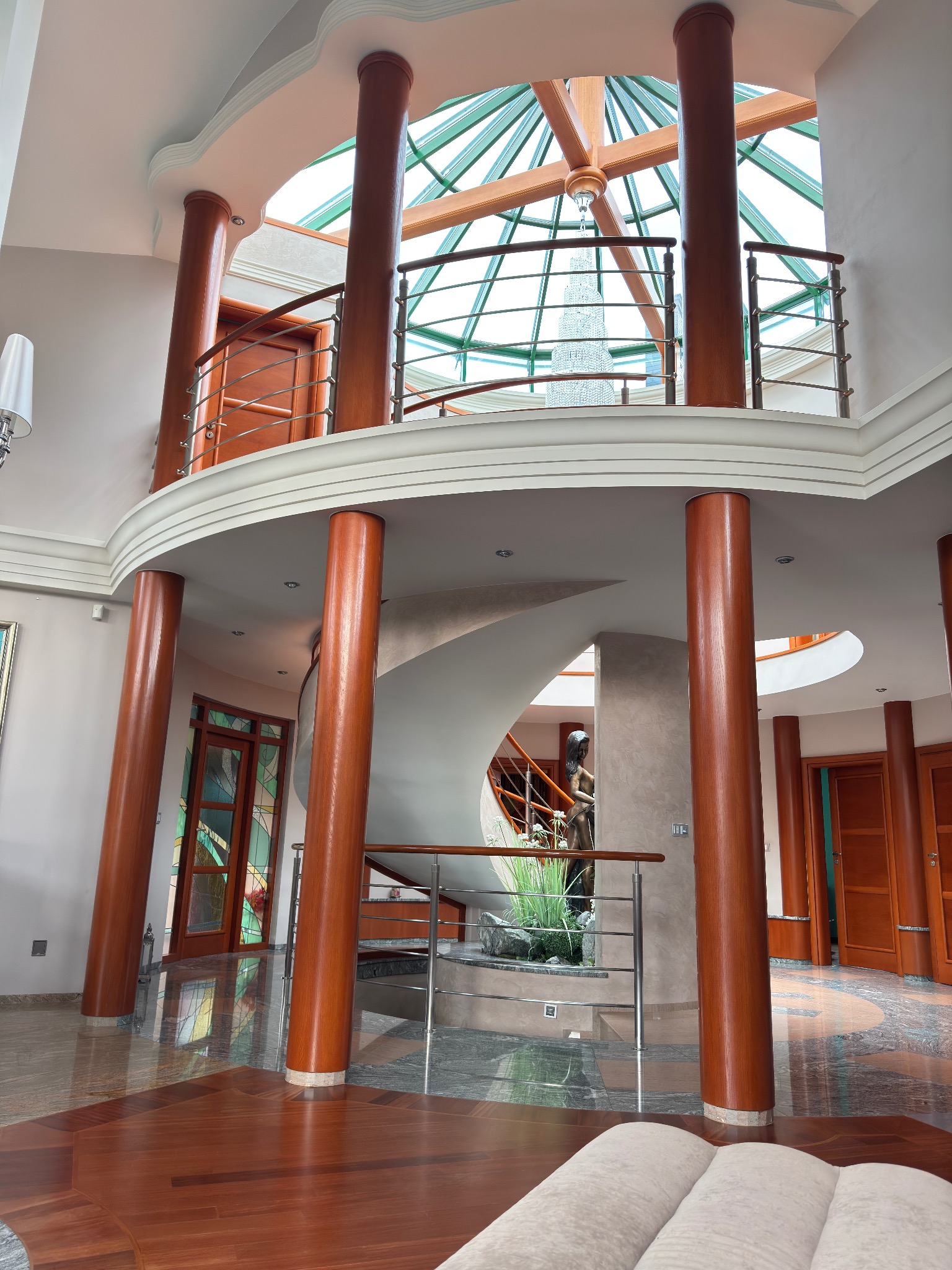 Dwupoziomowy hol z drewnianymi kolumnami, spiralnymi schodami, przeszklonym dachem i marmurową podłogą.