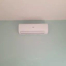 Biała jednostka klimatyzacyjna Haier zamontowana na pastelowo-zielonej ścianie w pomieszczeniu.