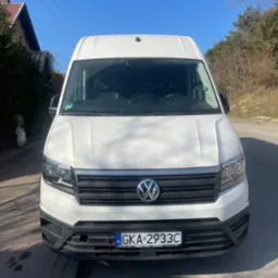 Biały Volkswagen Crafter zaparkowany na asfalcie, z widoczną tablicą rejestracyjną GKA 2933C i zieloną naklejką ekologiczną na szybie, sfotografowany w słoneczny dzień z perspektywy przodu pojazdu.