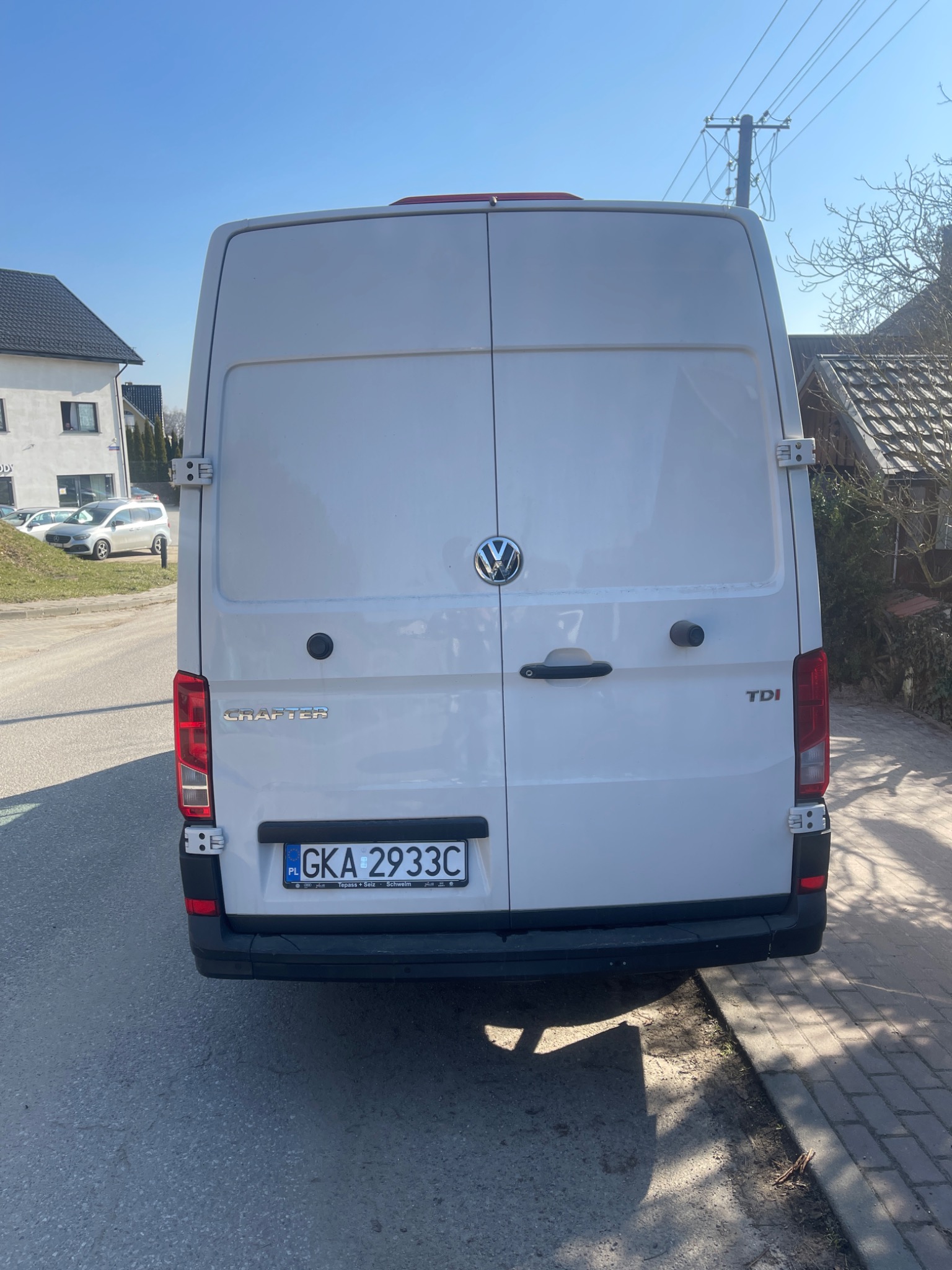 Tył białego samochodu dostawczego Volkswagen Crafter z polską tablicą rejestracyjną GKA 2933C, stojącego na ulicy w słoneczny dzień, widoczne budynki w tle.