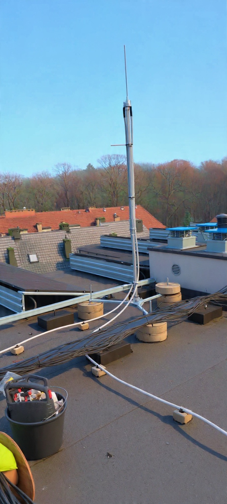 Zmontowana instalacja odgromowa na dachu budynku z widocznymi przewodami i elementami mocującymi. W tle drzewa i niebo.