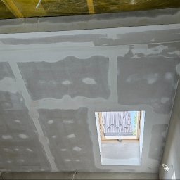 Renovo - Poddasze z oknem dachowym w trakcie prac wykończeniowych; widoczne łączenia płyt gipsowo-kartonowych wzmocnione taśmą i częściowo pokryte szpachlą, surowe ściany.