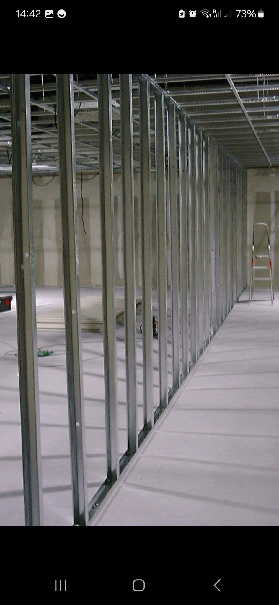 Metalowa konstrukcja szkieletowa pod zabudowę wewnątrz pomieszczenia, widoczny sufit podwieszany i drabina w tle.