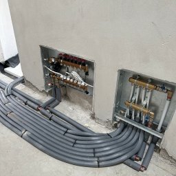 ARKADIUSZ NAWROCKI ZAKŁAD USŁUG INSTALACYJNYCH LECH-AR - Szare rury ogrzewania podłogowego w izolacji, prowadzone do rozdzielaczy w ścianie. Widoczne elementy instalacji i surowy stan wykończenia.