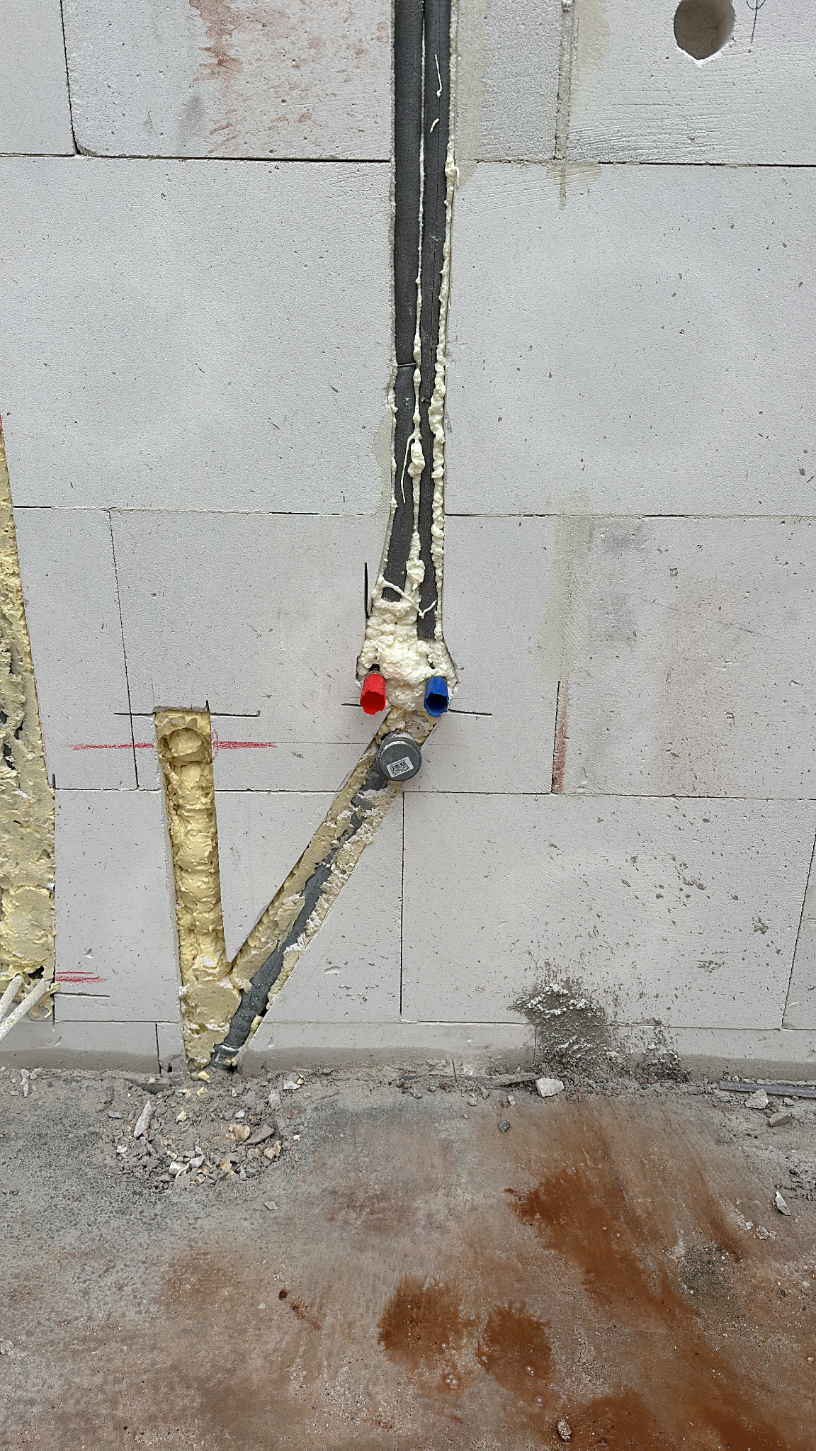 Instalacja rur w ścianie z betonu komórkowego, zabezpieczona pianką montażową. Widoczne końcówki rur z oznaczeniami kolorystycznymi.