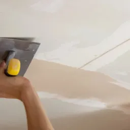 Nakładanie gładzi szpachlowej na łączenie płyt karton gips przy użyciu szpachelki z żółtą rączką.