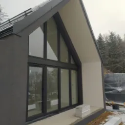 Nowoczesny dom jednorodzinny w Jeleniej Górze z dużymi oknami i szarą elewacją, częściowo ocieplony, z widocznymi materiałami budowlanymi na zewnątrz.