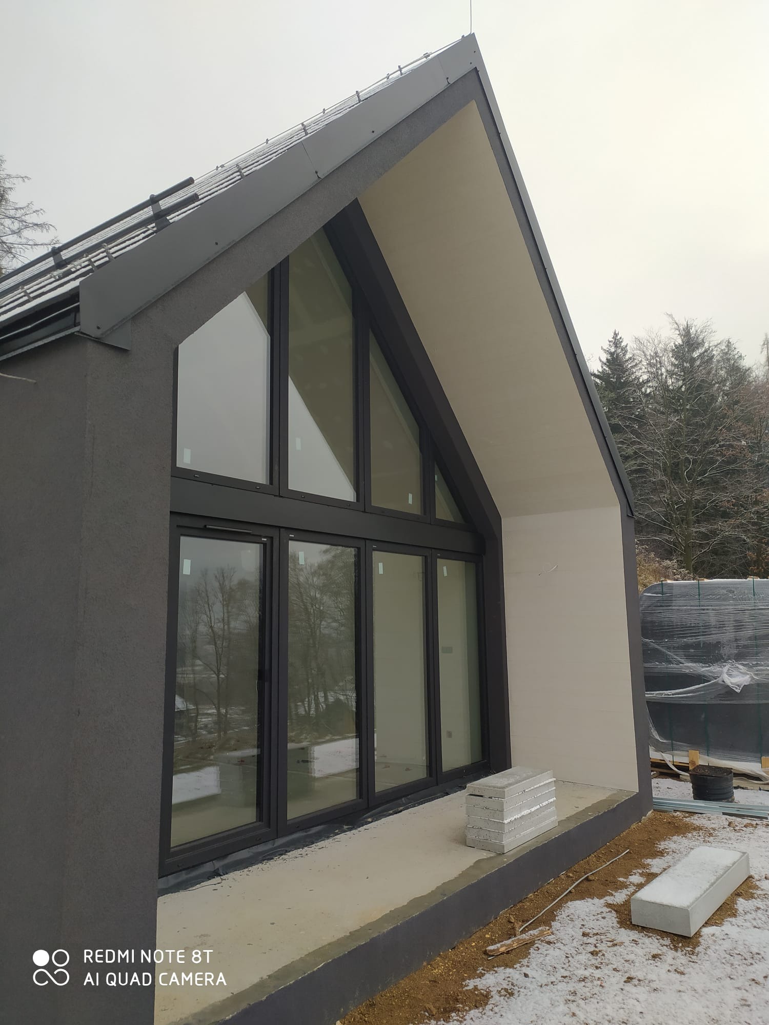 Nowoczesny dom jednorodzinny w Jeleniej Górze z dużymi oknami i szarą elewacją, częściowo ocieplony, z widocznymi materiałami budowlanymi na zewnątrz.