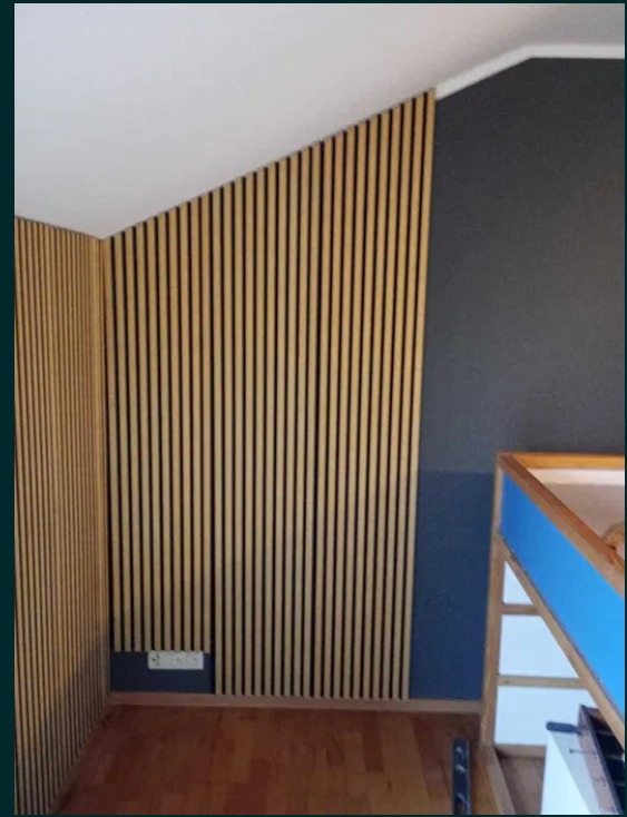 Ściana z paneli lamelowych w odcieniach beżu i czerni, zamontowana na skośnej ścianie w pokoju. Widoczna podłoga z paneli drewnianych i fragment ściany pomalowanej na ciemny kolor.
