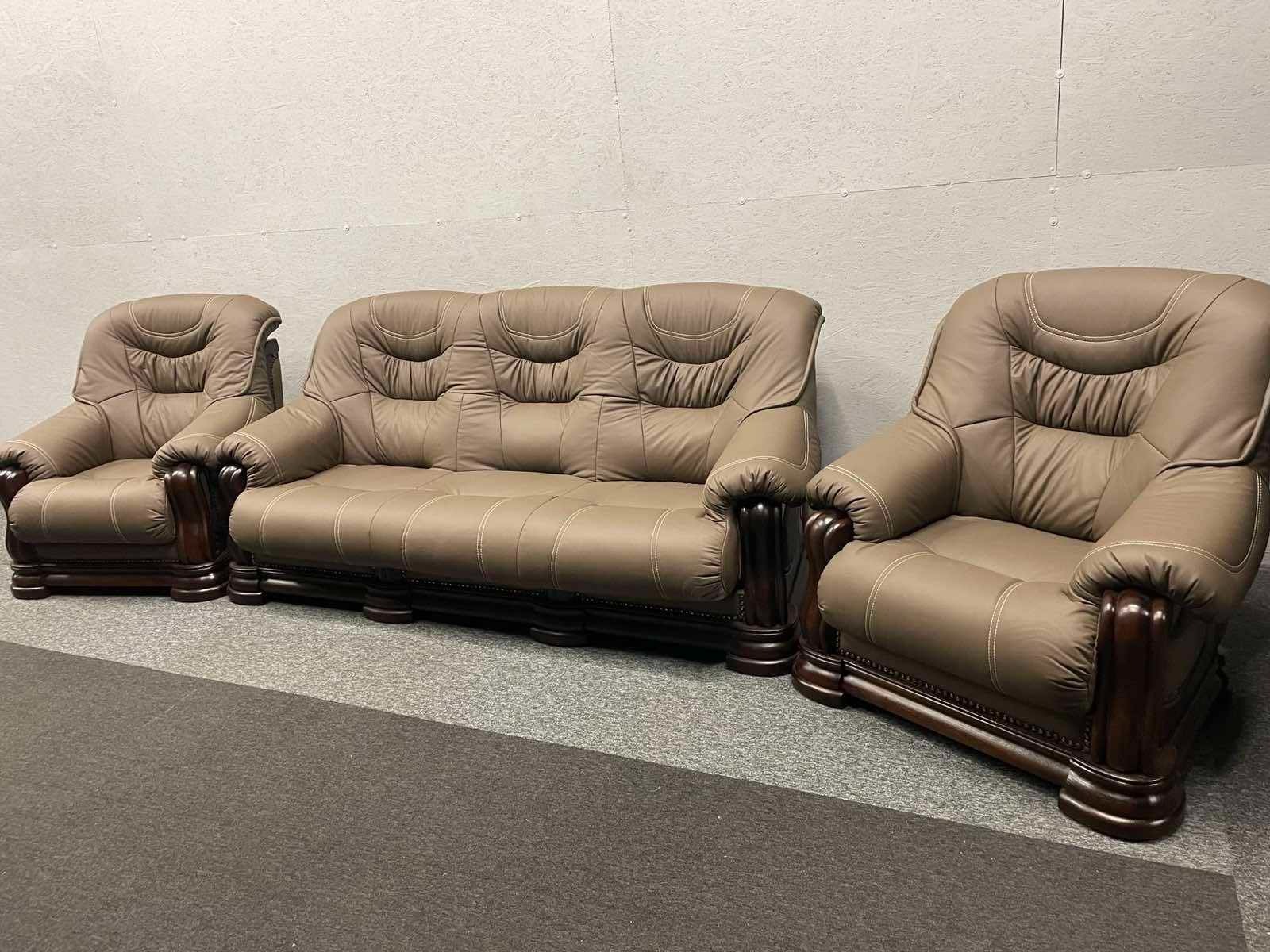 Komplet wypoczynkowy: brązowa, skórzana sofa trzyosobowa i dwa fotele z ciemnobrązowymi, drewnianymi zdobieniami, widoczne przeszycia jasną nicią.