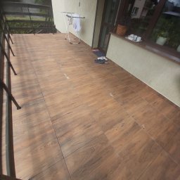 BESPBUD PAWEŁ PRZESTRZELSKI - Wyłożony brązowymi płytkami balkon z metalową balustradą, suszarką na pranie i parą butów przy oknie.