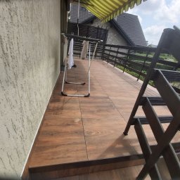 BESPBUD PAWEŁ PRZESTRZELSKI - Balkon z drewnopodobnymi płytkami, szarym tynkiem strukturalnym na ścianie i rozkładaną suszarką na pranie, widok z góry na zewnątrz.