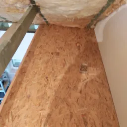 Płyta OSB zamontowana na poddaszu, widoczna izolacja z wełny mineralnej, drewniane belki konstrukcyjne i pojemnik z wkrętami.