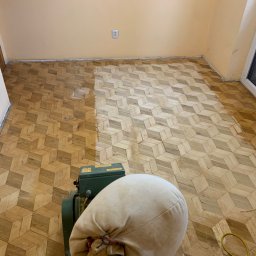 HOME Parkiet Cyklinowanie podłóg, montaż schodów, zabudowy stolarskie Maciej Wojciechowski - Parkiet w geometryczny wzór, częściowo odnowiony maszyną do cyklinowania, widoczny worek na pył i kabel zasilający.