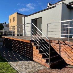 Augustowiak - Zewnętrzne schody drewniane z metalową balustradą na tarasie przy nowoczesnym domu w słoneczny dzień.