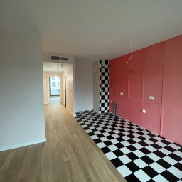 STYL-NOV SERHII BYNCHUK - Wnętrze mieszkania w trakcie wykańczania: połączenie drewnianej podłogi, czarno-białej szachownicy na ścianie i podłodze oraz ściany w odcieniach różu z dekoracyjnymi panelami.