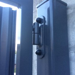 GKDSpaw - Szczegół zawiasu na słupku bramy wjazdowej, widok z bliska, szara farba, betonowy słupek.