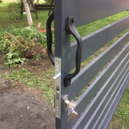 GKDSpaw - Szara, pozioma brama wjazdowa z czarną klamką i zamkiem z kluczem, na tle zielonego trawnika i drzew