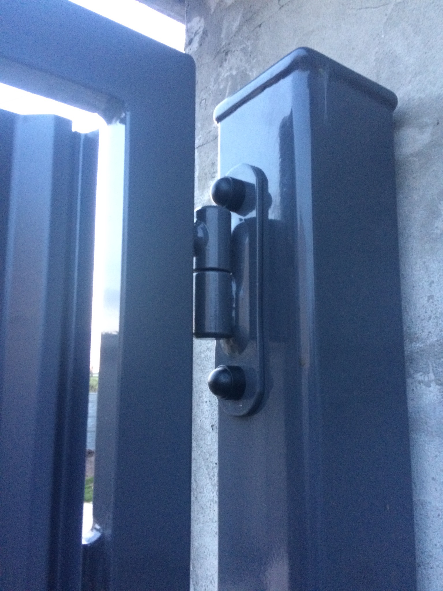 Szczegół zawiasu na słupku bramy wjazdowej, widok z bliska, szara farba, betonowy słupek.