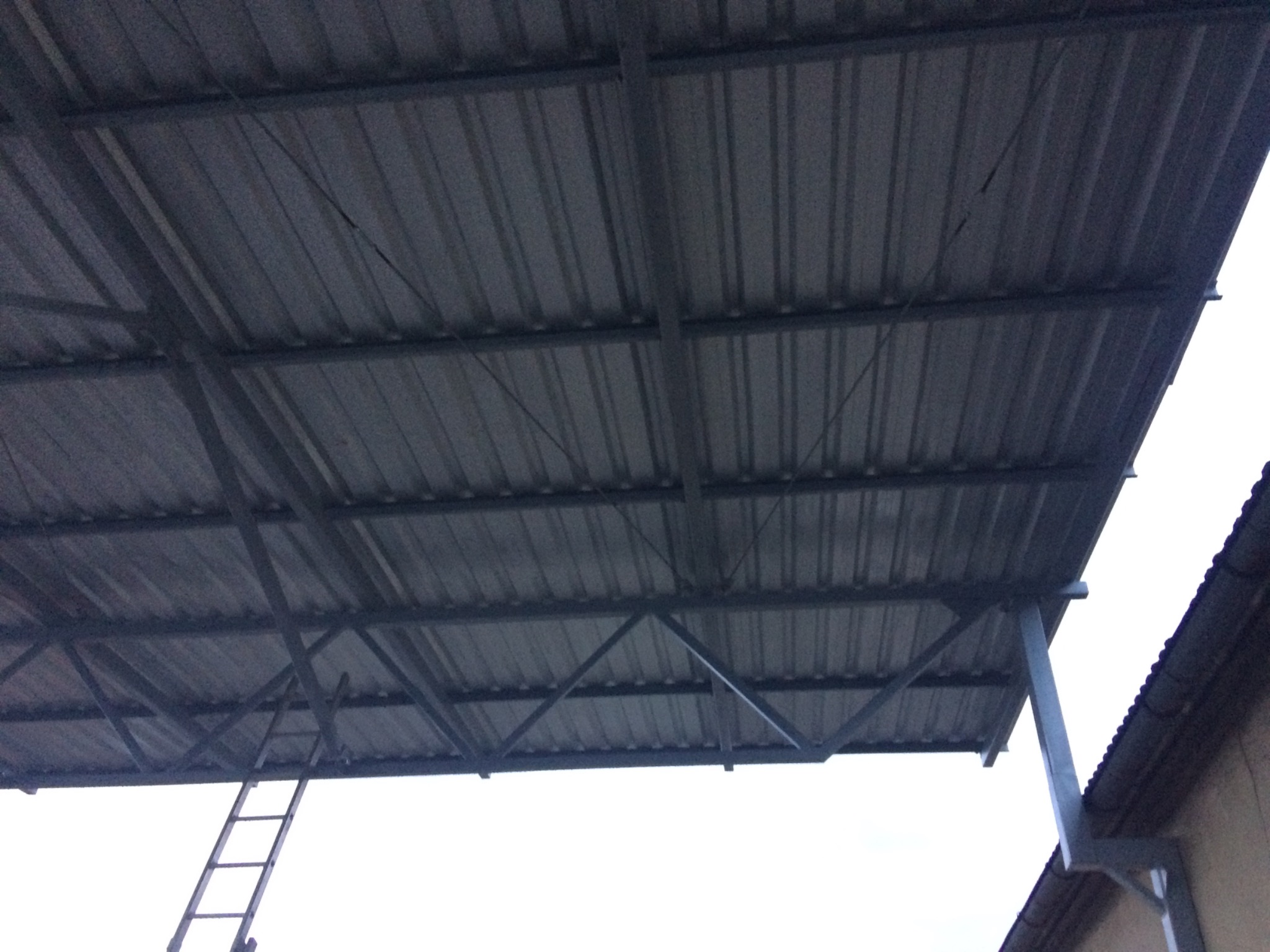 Konstrukcja z metalowych profili z blachą trapezową, prawdopodobnie zadaszenie, widok od spodu z fragmentem drabiny w lewym dolnym rogu.