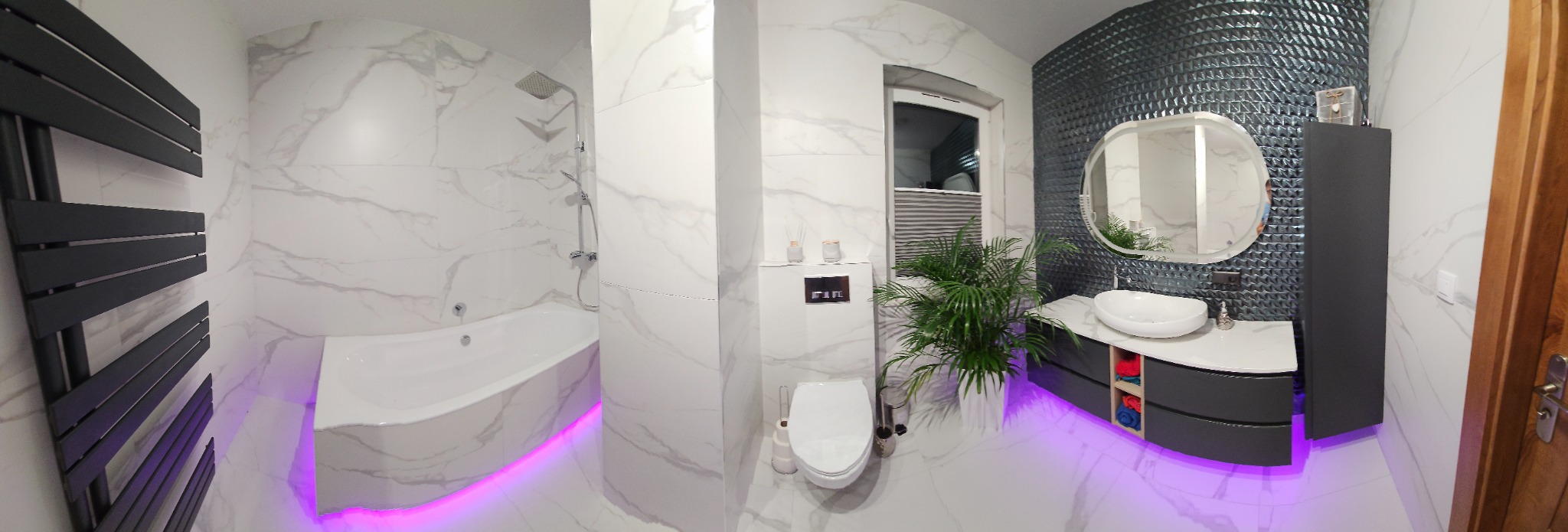 Nowoczesna łazienka z marmurowymi płytkami, podświetlaną wanną, umywalką nablatową, dekoracyjną ścianą i czarnym grzejnikiem.