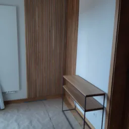 Panel dekoracyjny z drewnianych listew na ścianie w jasnym wnętrzu, obok konsola z metalowym stelażem i drewnianymi półkami.