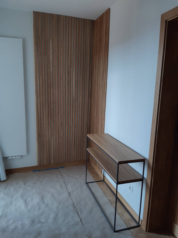 Panel dekoracyjny z drewnianych listew na ścianie w jasnym wnętrzu, obok konsola z metalowym stelażem i drewnianymi półkami.