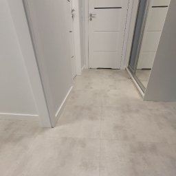 Good home - Wykończony korytarz z szarymi płytkami podłogowymi, białymi drzwiami z czarnymi akcentami i zabudowaną szafą z lustrem.