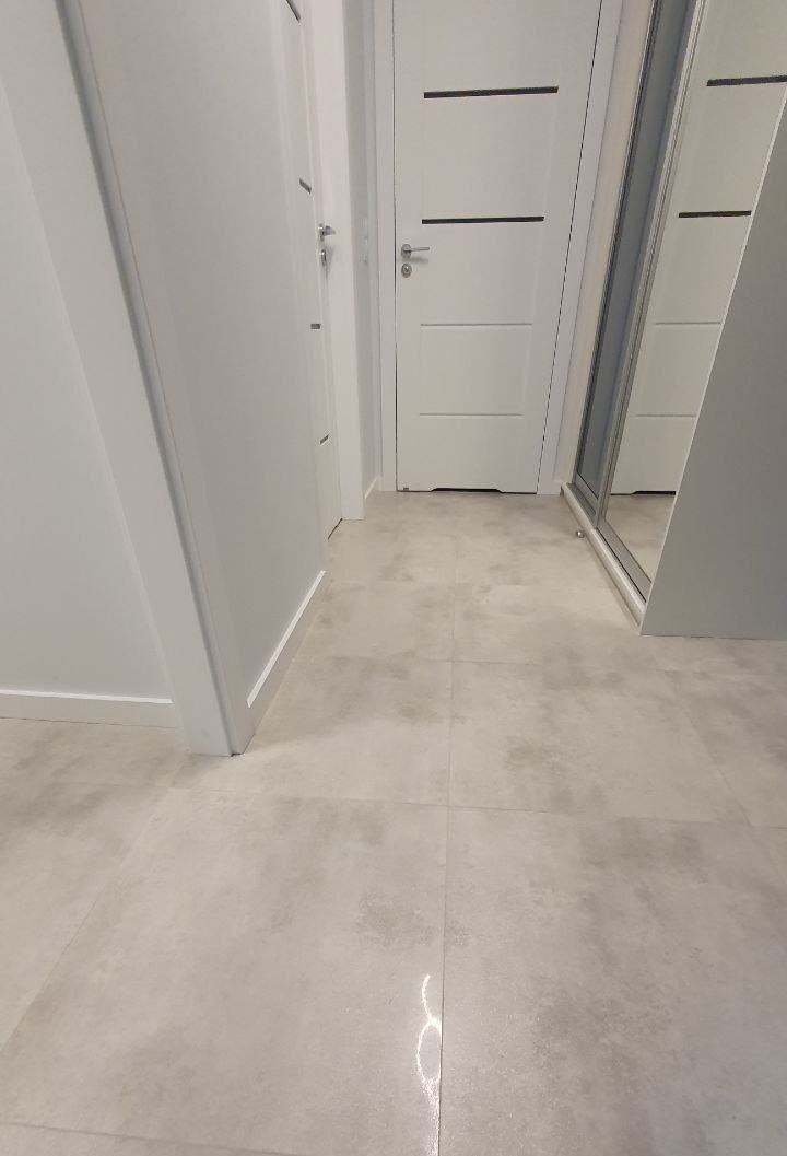 Wykończony korytarz z szarymi płytkami podłogowymi, białymi drzwiami z czarnymi akcentami i zabudowaną szafą z lustrem.