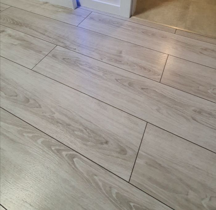 Ułożona podłoga z paneli imitujących jasne drewno, widoczne fugi i fragment progu.