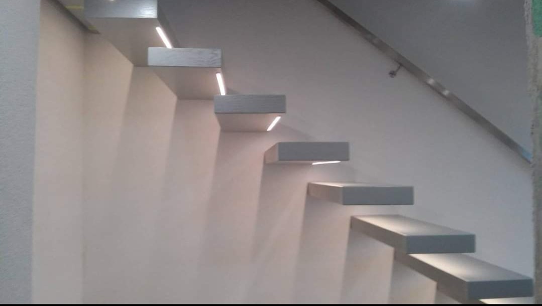 Nowoczesne schody wspornikowe z podświetleniem LED od spodu stopni, stalowa poręcz przymocowana do ściany.