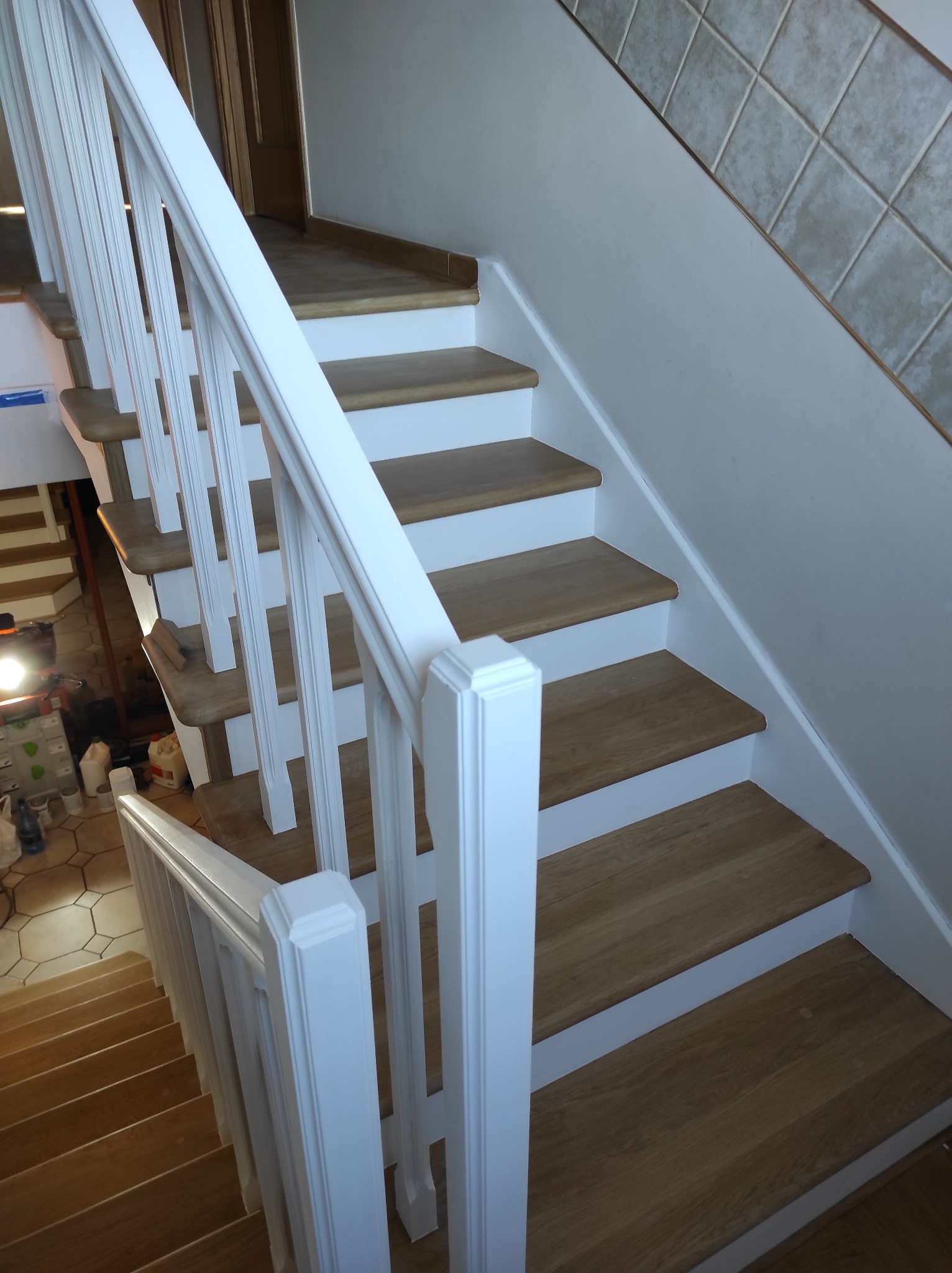 Odnowione schody drewniane z białymi balustradami, widoczne narzędzia i materiały w tle, jasna kolorystyka.