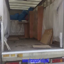 Wnętrze meblowozu wypełnione zabezpieczonymi meblami, kartonami i workami, przygotowane do transportu. Widoczne zabezpieczenia folią bąbelkową oraz elementy drewniane mebli. Na tylnej klapie...