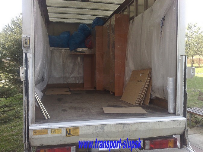 Wnętrze meblowozu wypełnione zabezpieczonymi meblami, kartonami i workami, przygotowane do transportu. Widoczne zabezpieczenia folią bąbelkową oraz elementy drewniane mebli. Na tylnej klapie...