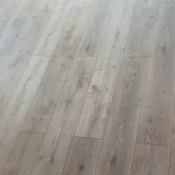 Ułożone panele podłogowe w odcieniach szarości z widoczną szczotką do zamiatania w lewym górnym rogu i niedokończonym wykończeniem przy ścianie po prawej stronie.