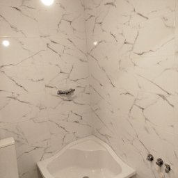 ANDRZEJ RICHTER - Biała łazienka z marmurowymi płytkami, narożną wanną i chromowaną armaturą. Widoczne detale wykończenia, takie jak uchwyt na ręcznik i zawory.