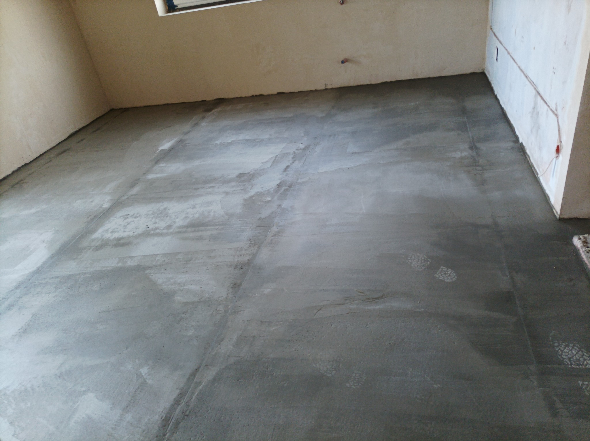 Wylana, świeża posadzka w pomieszczeniu w Kazimierzy Wielkiej. Widoczne ślady butów na mokrym betonie. Przygotowanie do dalszych prac wykończeniowych.